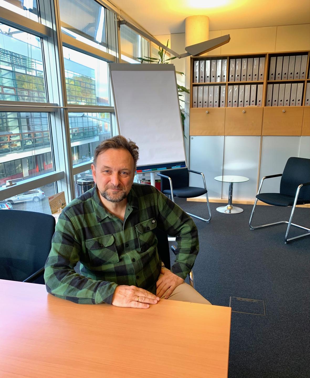 Ein Mann sitzt an einem Tisch in einem Büro und schaut freundlich in die Kamera: der Business-Coach Eckart Fiolka