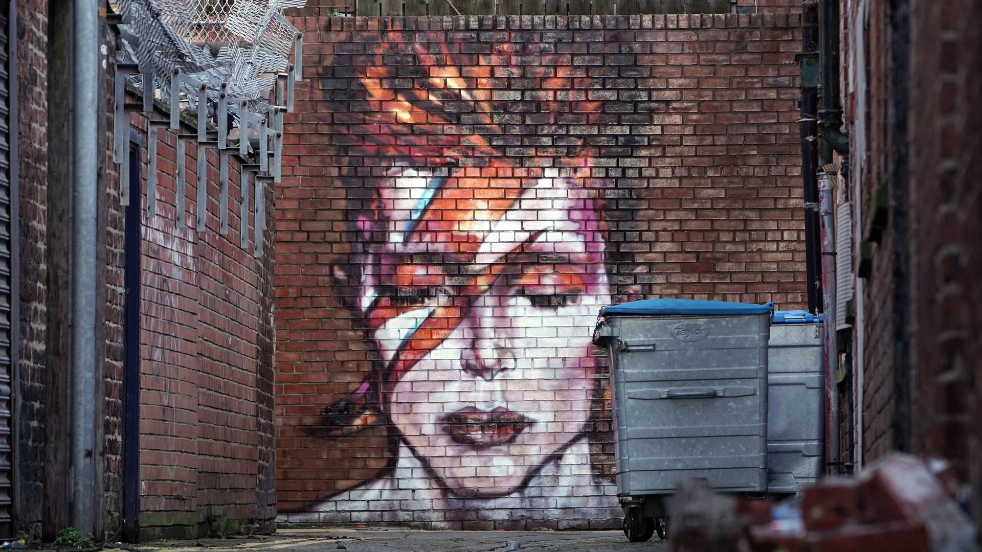 Ein Graffito in einem Hinterhof zeigt David Bowie mit geschlossenen Augen und den für ihn typischen Blitz im Gesicht. Ein Graffito in einem Hinterhof zeigt David Bowie mit geschlossenen Augen und den für ihn typischen Blitz im Gesicht.