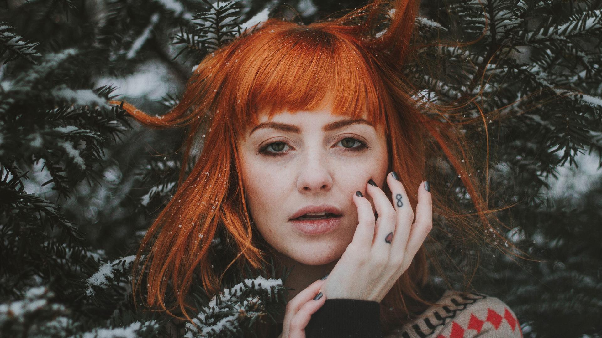 Das Gesicht einer jungen, rothaarigen Frau ist von verschneiten Tannenzweigen umgeben.