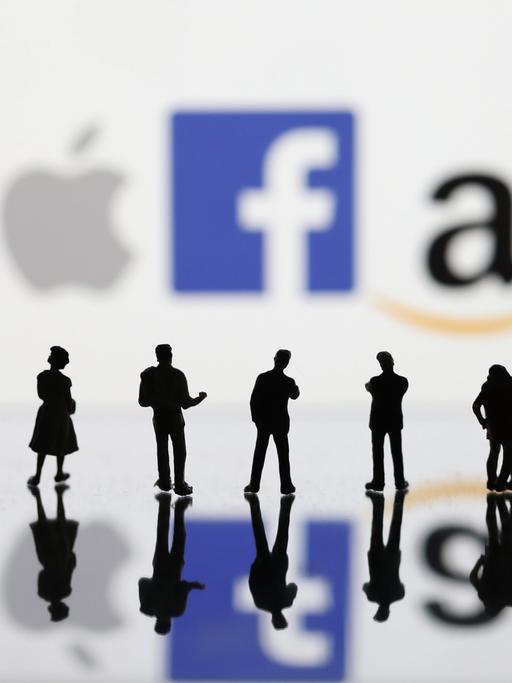 Ein Symbolbild zeigt Umrisse von Menschen (Figuren), die vor den Logos der großen Digitalkonzerne Google, Apple, Facebook und Amazon stehen 