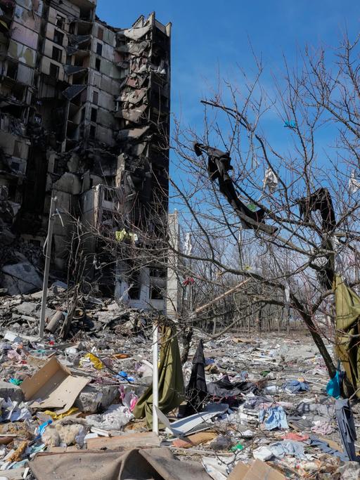 Kleidung, die durch russischen Beschuss aus einem ausgebrannten Haus in Charkiw in der Ostukraine auf einen Baum geschleudert wurde, und dahinter das bombardierte Haus am 26. März 2022.
