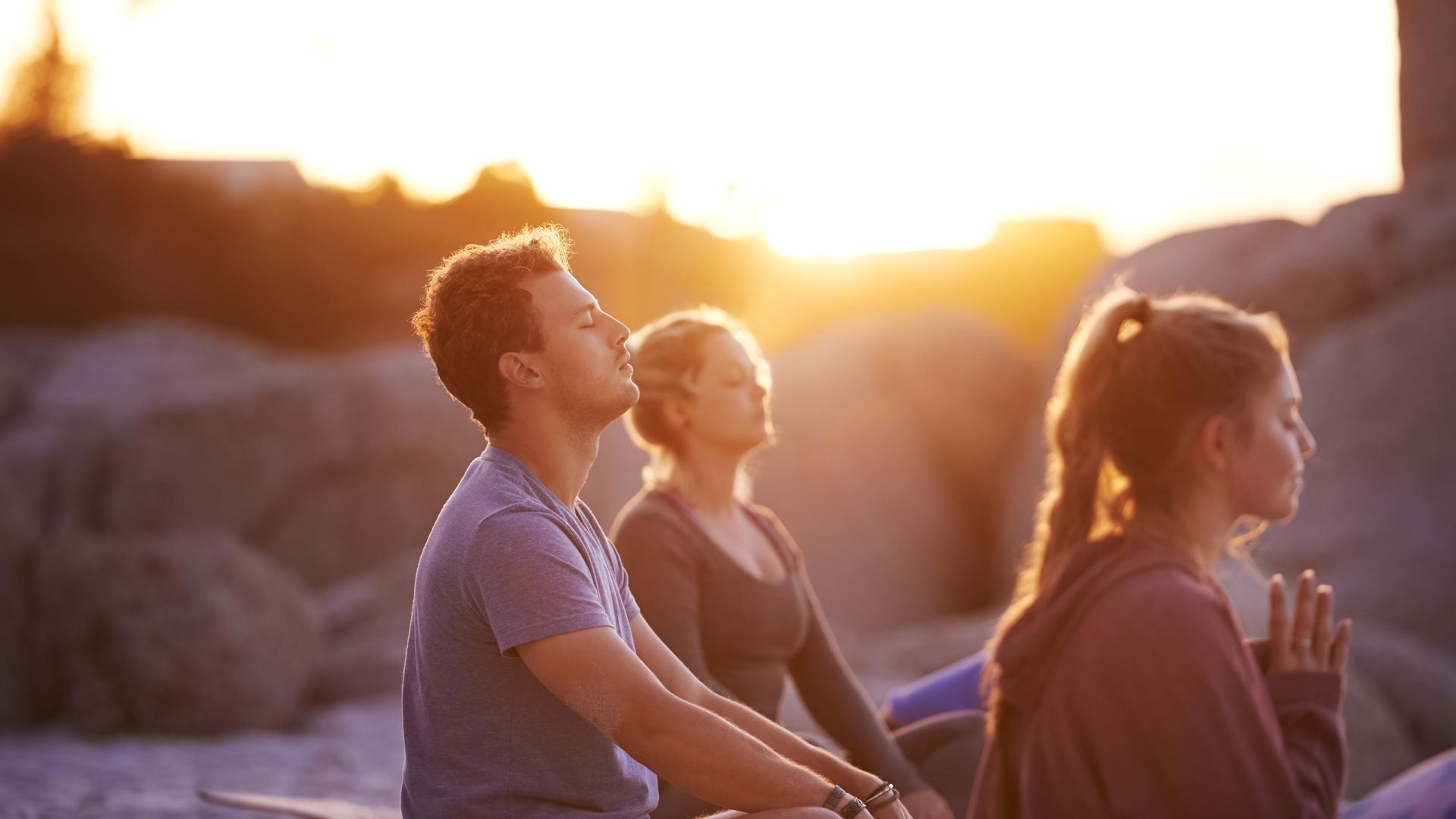 Drei junge Menschen meditieren, im Hintergrund goldenes Licht. Drei junge Menschen meditieren, im Hintergrund goldenes Licht.