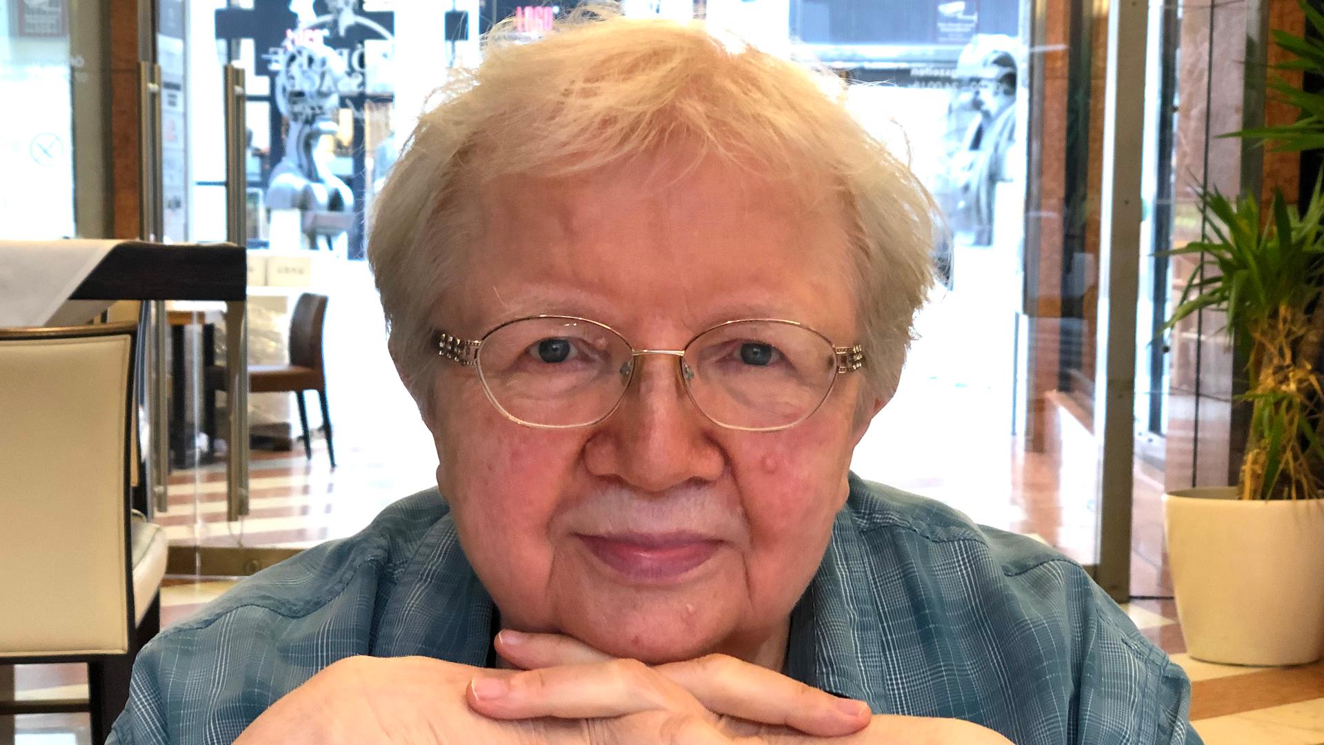 Luise F. Pusch. Eine ältere Frau mit Brille und kurzen Haaren sitzt an einem Tisch. Luise F. Pusch. Eine ältere Frau mit Brille und kurzen Haaren sitzt an einem Tisch.
