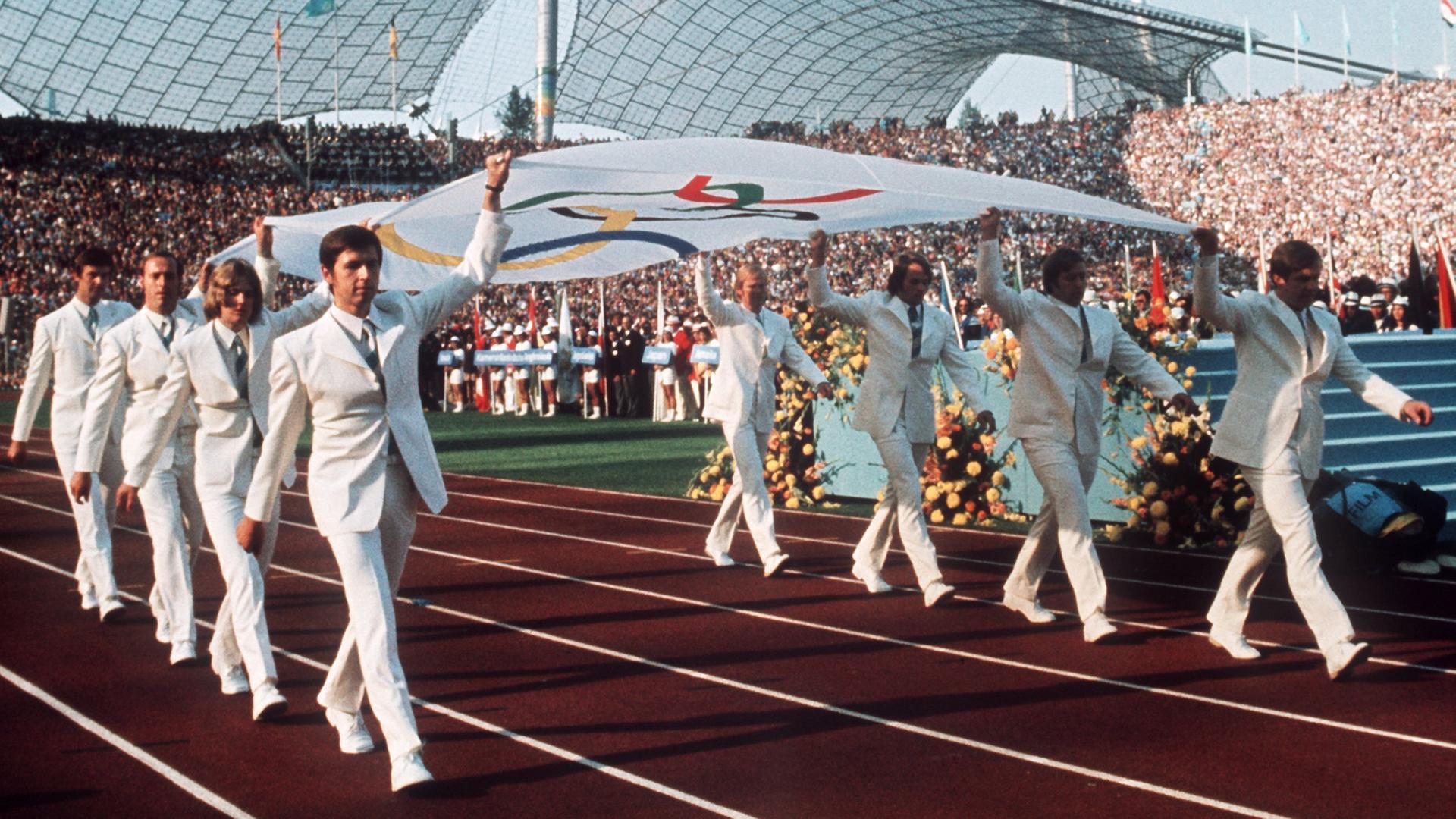 Die Mannschaft des deutschen Gold-Achters (Rudern) von Mexiko 1968 trägt die Olympische Fahne feierlich in das Münchener Olympiastadion während der Eröffnungsfeier der Olympischen Sommerspiele am 26. August 1972.