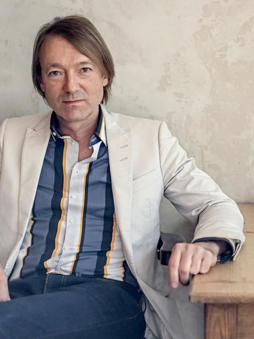 Musiker Jochen Distelmeyer sitzt an einem Holztisch vor einer Wand.