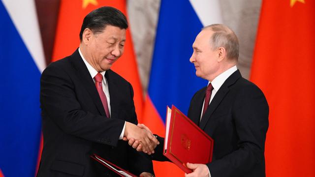Das Foto zeigt Chinas Präsident Xi Jinping und Russlands Präsident Wladimir Putin. Sie schütteln vor ihren Staatsflaggen die Hände und halten zugleich Verträge hoch.