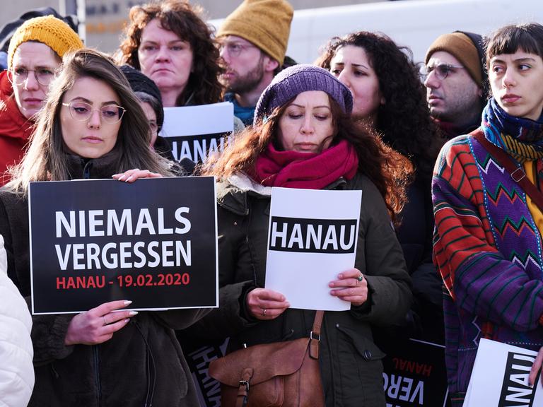 "Hanau" und "Niemals vergessen" steht auf den Schildern, die ein Chor bei der Gedenkveranstaltung eines Bündnisses von Initiativen und Organisationen auf dem Oranienplatz hält. Ein 43-jähriger Deutscher hatte am 19. Februar 2020 in Hanau neun Menschen aus rassistischen Motiven ermordet.