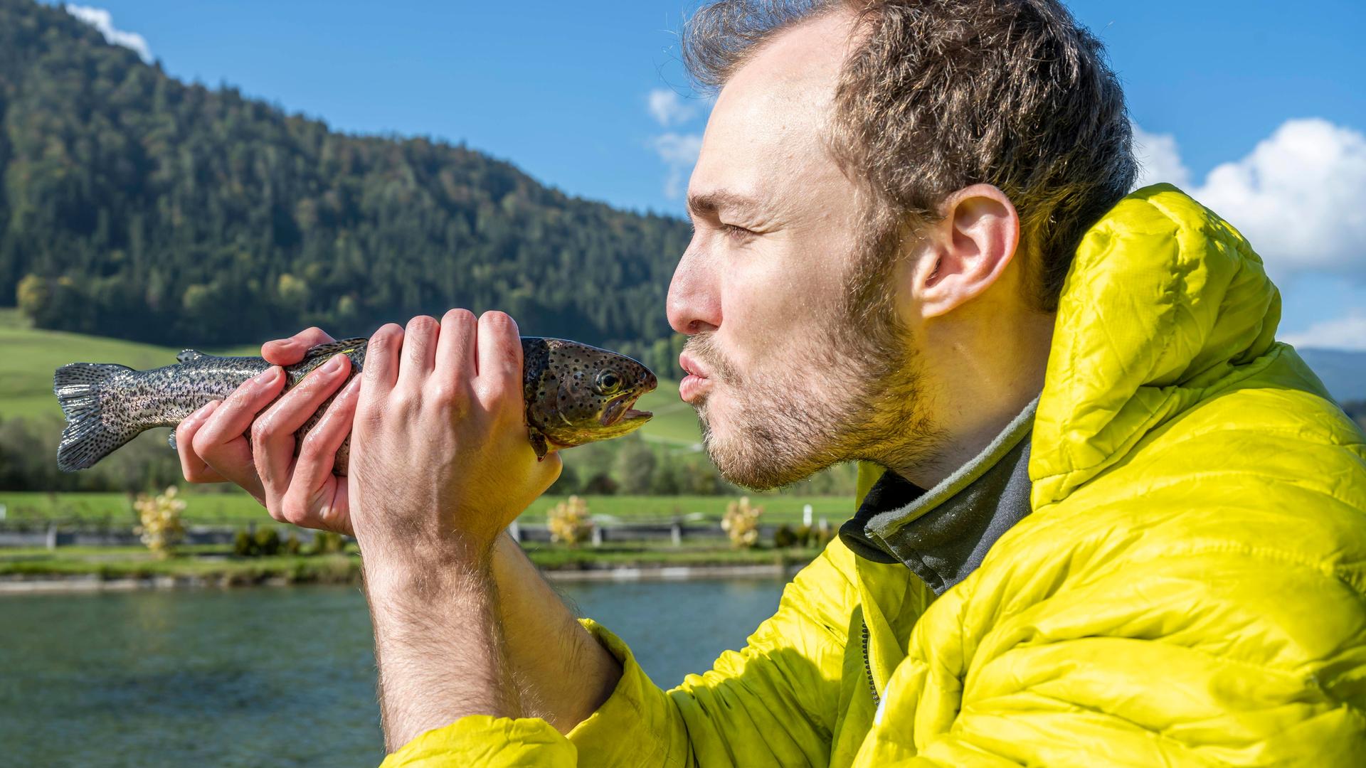 Ein Mann hält einen Fisch vor sein Gesicht und deutet einen Kuss an. Ein Mann hält einen Fisch vor sein Gesicht und deutet einen Kuss an.