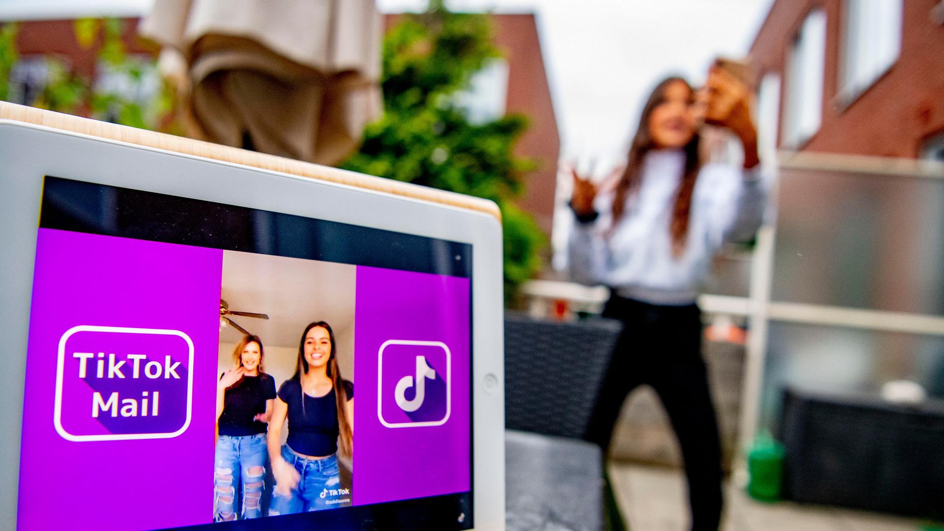 Ein Mädchen tanzt im unscharfen Bildhintergrund für ein Tiktok-Video. In der Hand hält sie ein Handy, im Vordergrund ein Computer mit TikTok-Oberfläche. Ein Mädchen tanzt im unscharfen Bildhintergrund für ein Tiktok-Video. In der Hand hält sie ein Handy, im Vordergrund ein Computer mit TikTok-Oberfläche.
