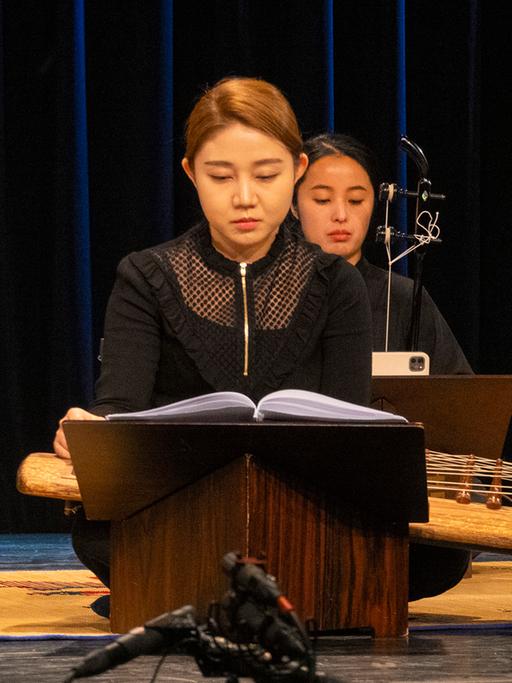 Drei Musikerinnen mit traditionellen koreanischen Instrumenten sitzen mit kontrollierten Blicken auf der Bühne