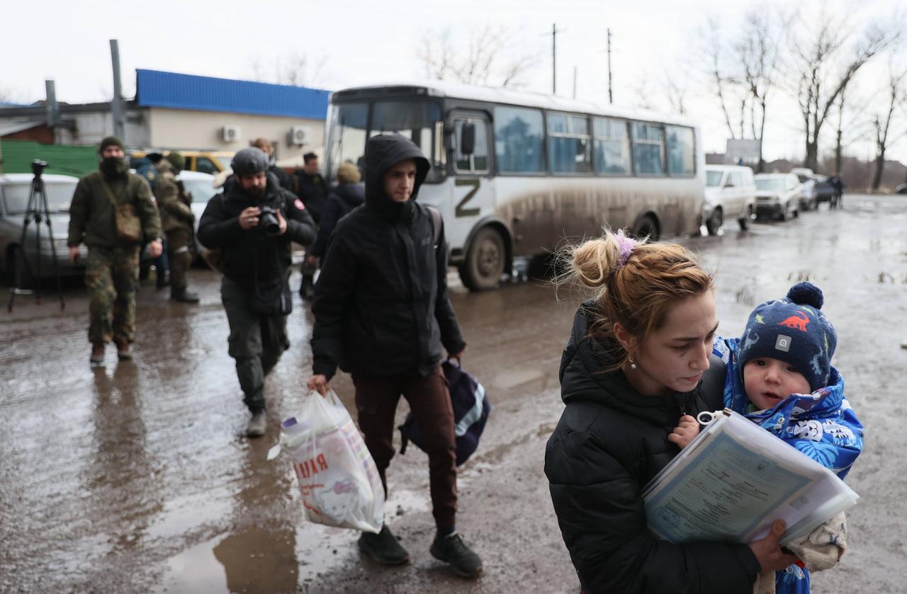 Flüchtlinge, die Mariupol verlassen haben, steigen in der Stadt Bezymennoye aus einem Bus aus. Im Vordergrund eine Mutter mit einem Kleinkind auf dem Arm, dahinter Männer mit Taschen.