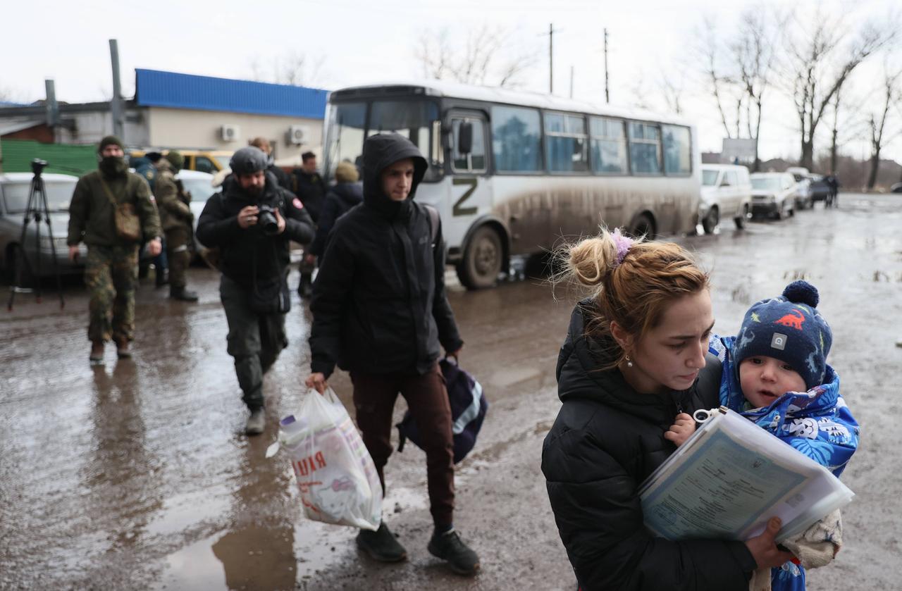 Flüchtlinge, die Mariupol verlassen haben, steigen in der Stadt Bezymennoye aus einem Bus aus. Im Vordergrund eine Mutter mit einem Kleinkind auf dem Arm, dahinter Männer mit Taschen. Flüchtlinge, die Mariupol verlassen haben, steigen in der Stadt Bezymennoye aus einem Bus aus. Im Vordergrund eine Mutter mit einem Kleinkind auf dem Arm, dahinter Männer mit Taschen.