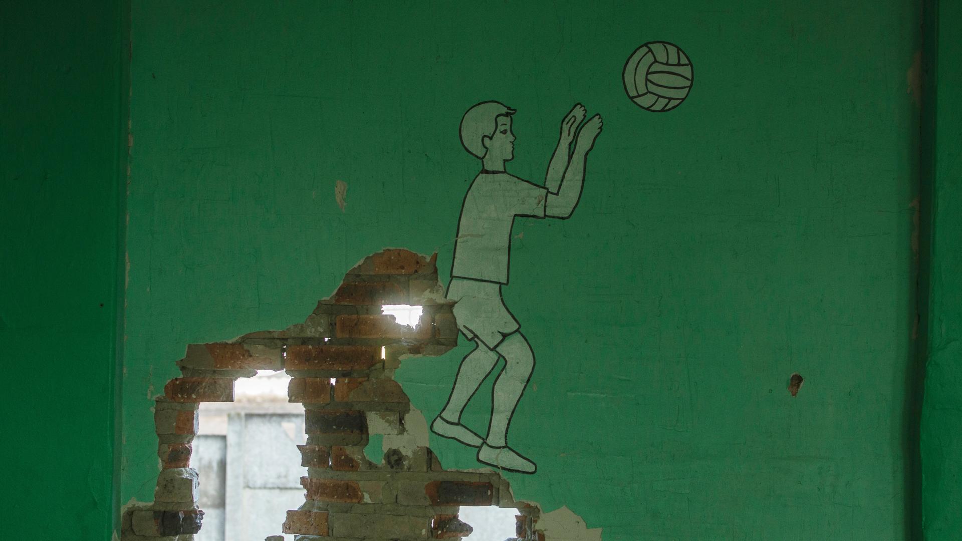 Eine durch militärischen Beschuss durchlöcherte Wand in einer Schule in Bakhmut, Gebiet Donezk. Auf der grünen Wand ist ein Junge beim Ball spielen abgebildet.