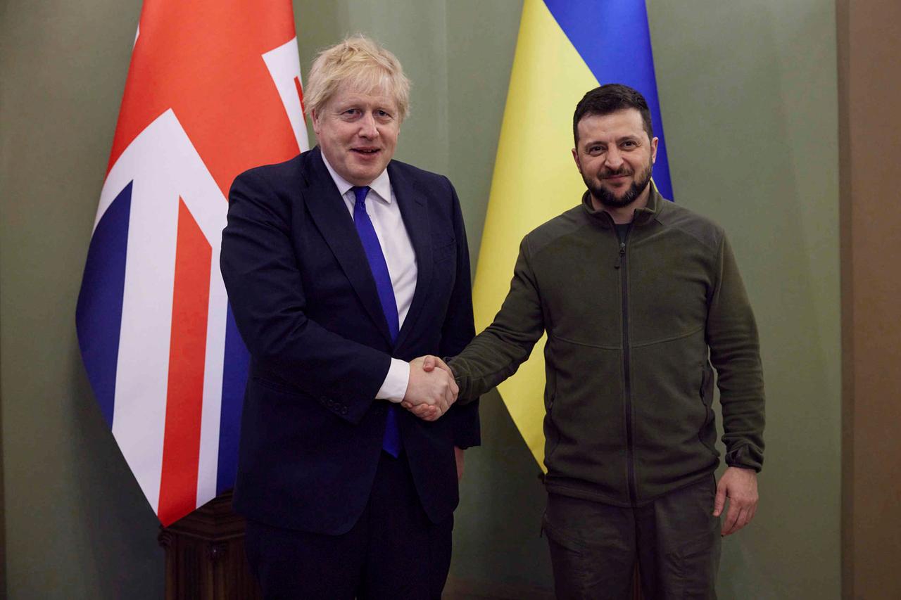 Zwei Männer schütteln sich die Hand. Im Hintergrund sind die britische und die ukrainische Fahne zu sehen.