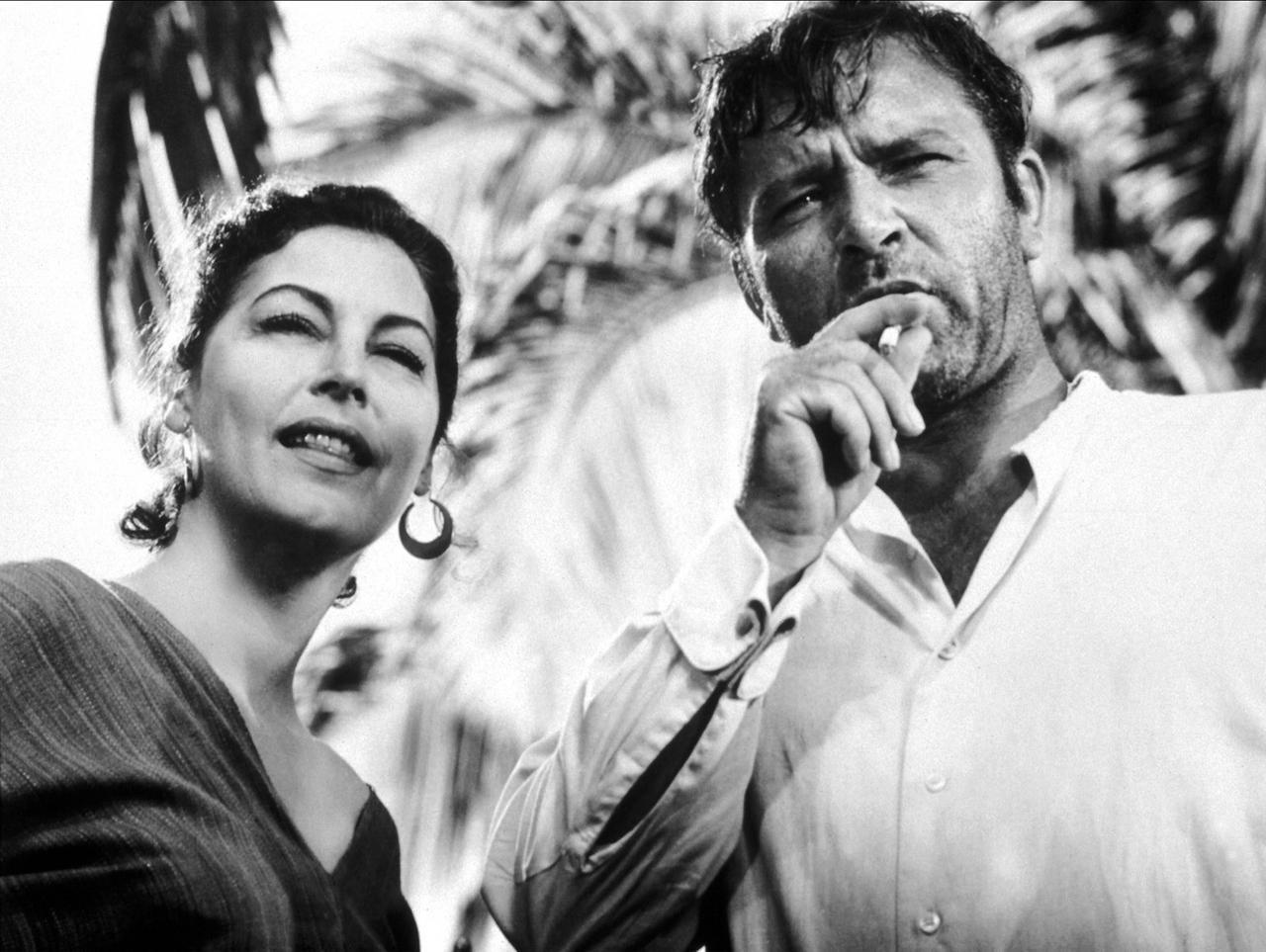 Szene aus dem Film "Die Nacht des Leguan": Ava Gardner und der Zigarette rauchende Richard Burton stehen nebeneinander und schauen nach vorne Szene aus dem Film "Die Nacht des Leguan": Ava Gardner und der Zigarette rauchende Richard Burton stehen nebeneinander und schauen nach vorne