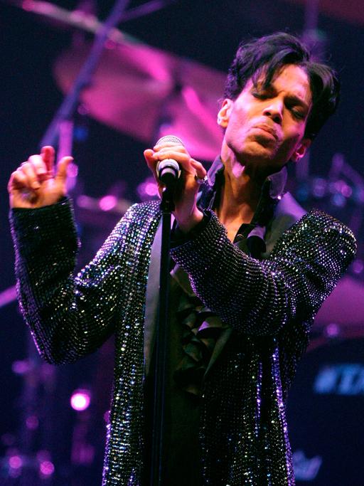 Der Sänger Prince mit geschlossen Augen und einem Mikrofon in der Hand beim Auftritt auf der Bühne.