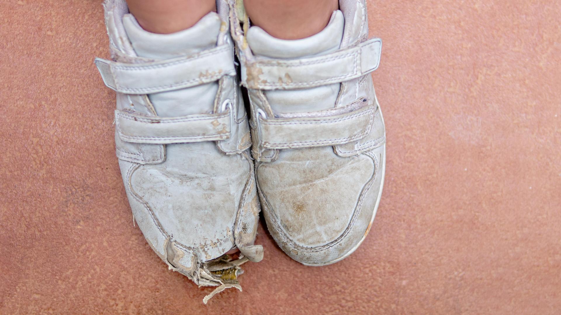 Kinderfüße in kaputten weißen Sportschuhen, die vorne ein Loch haben. Kinderfüße in kaputten weißen Sportschuhen, die vorne ein Loch haben.