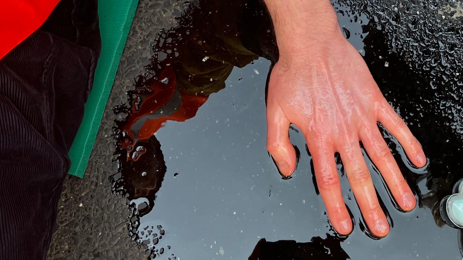 Ein Klima-Aktivist hat seine Hand auf einer Straße festgeklebt. 
