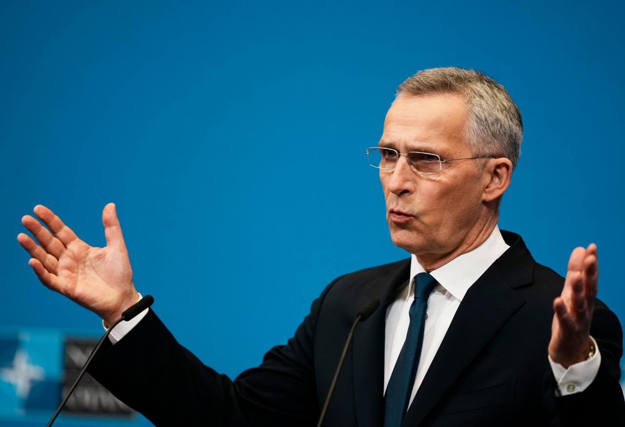 Ein Mann in dunklem Anzug hält die Arme ausgebreitet und spricht vor einem blauen Hintergrund. Ein Mann in dunklem Anzug hält die Arme ausgebreitet und spricht vor einem blauen Hintergrund.