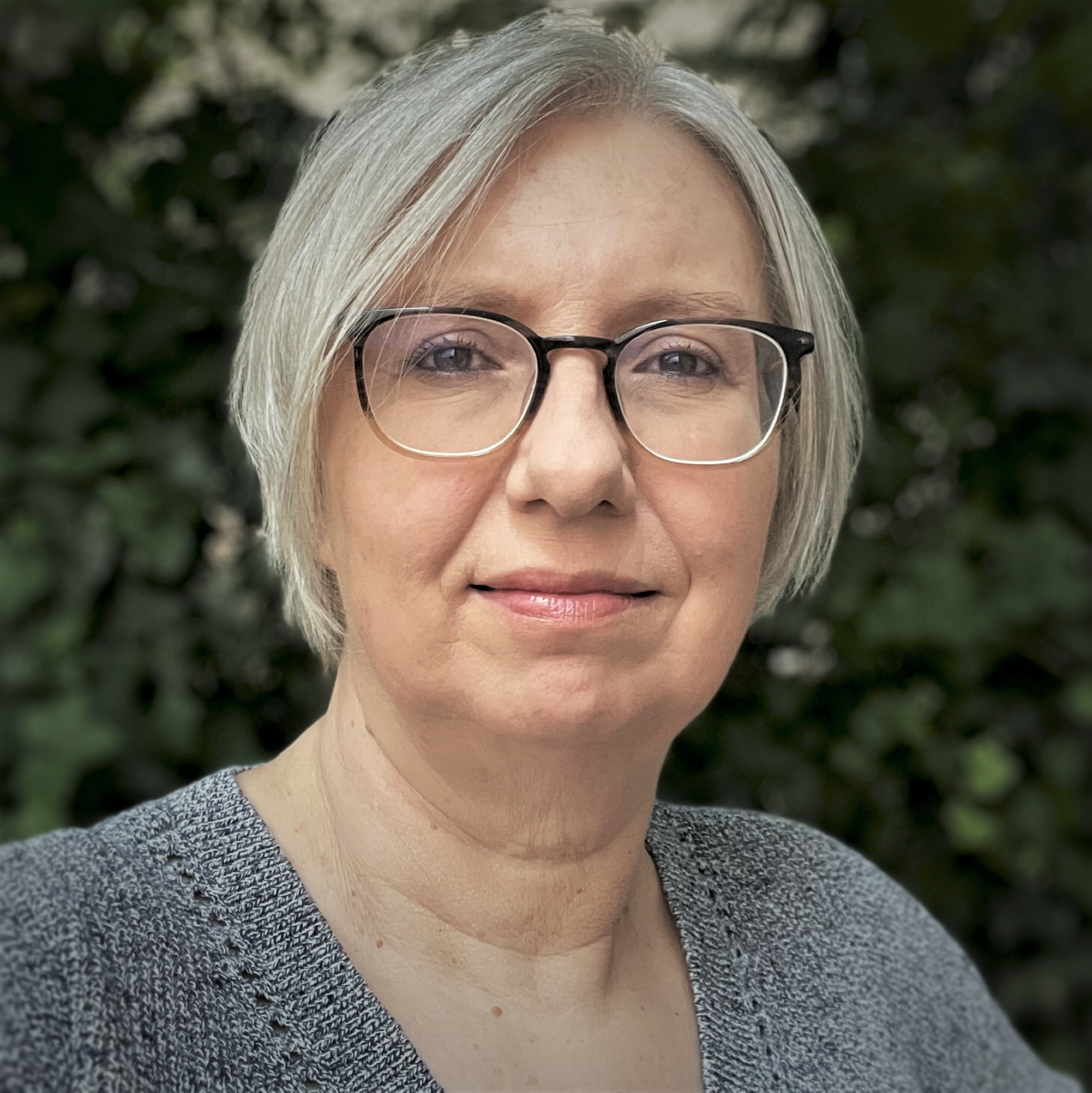 Antje Schrupp trägt einen grauen Strickpullover und steht im Freien vor einer Hecke. Antje Schrupp trägt einen grauen Strickpullover und steht im Freien vor einer Hecke.