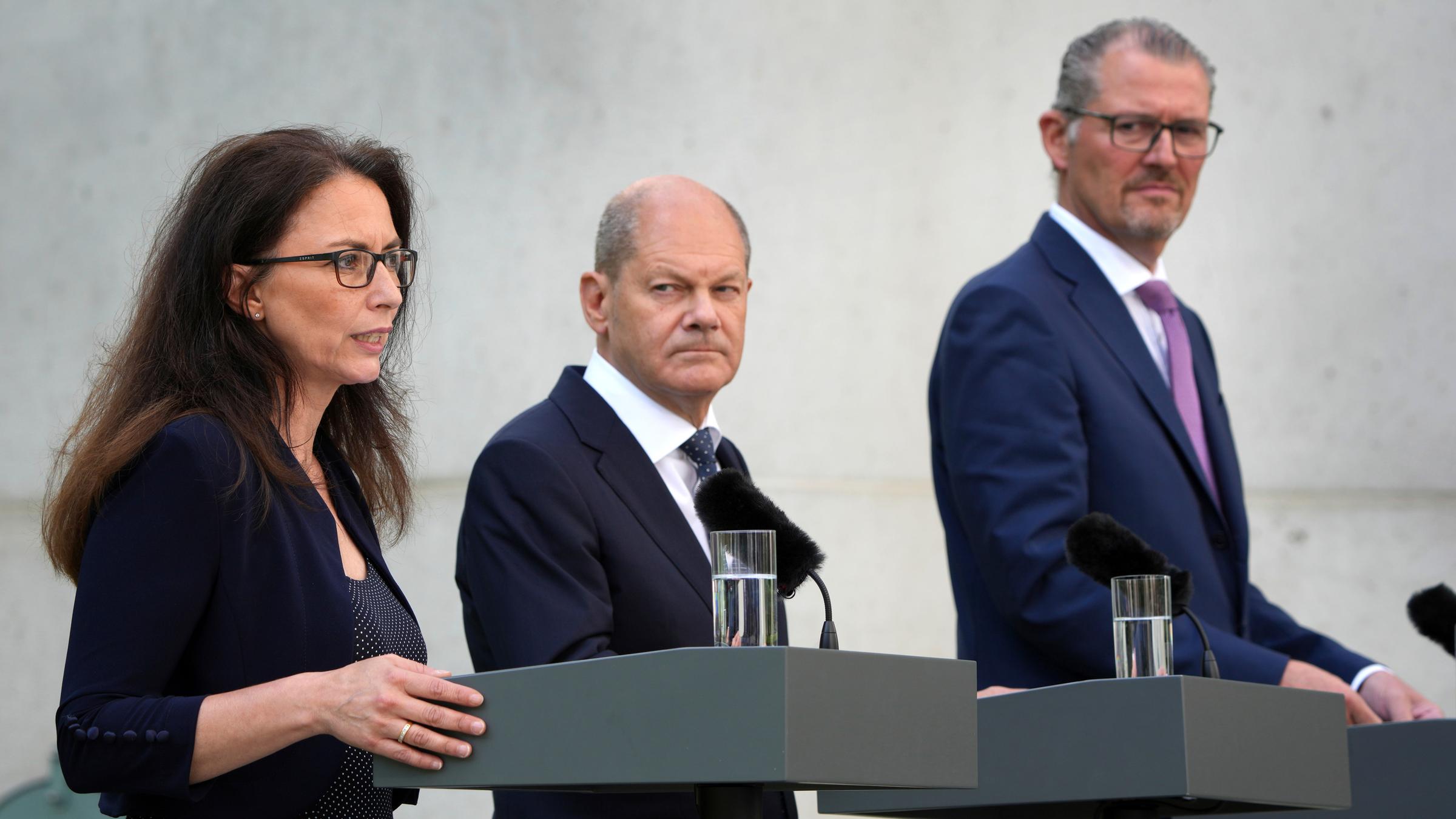 Yasmin Fahimi, Olaf Scholz und Rainer Dulger stehen an jeweils einem Rednerpult. 