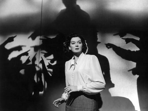 Rosalind Russell in einer Filmszene ca. 1947, in der mehrere Handschatten auf sie zeigen und sie umzingeln. 