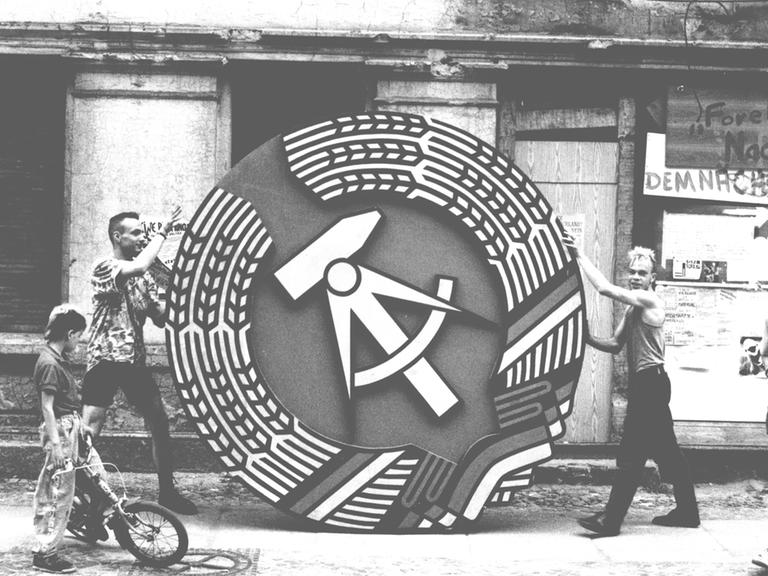 Zwei Männer halten ein Symbol der DDR 