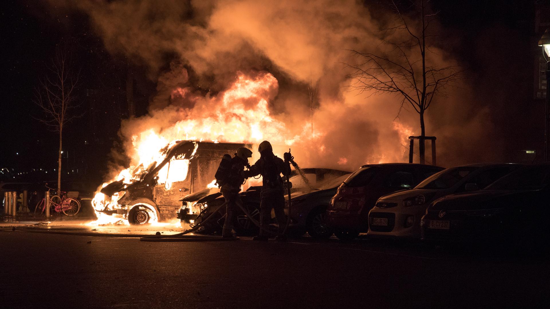 Feuerwehrleute versuchen ein brennendes Auto zu löschen. Es ist Nacht und alles ist sehr dunkel, nur das Feuer sticht hervor. Feuerwehrleute versuchen ein brennendes Auto zu löschen. Es ist Nacht und alles ist sehr dunkel, nur das Feuer sticht hervor.