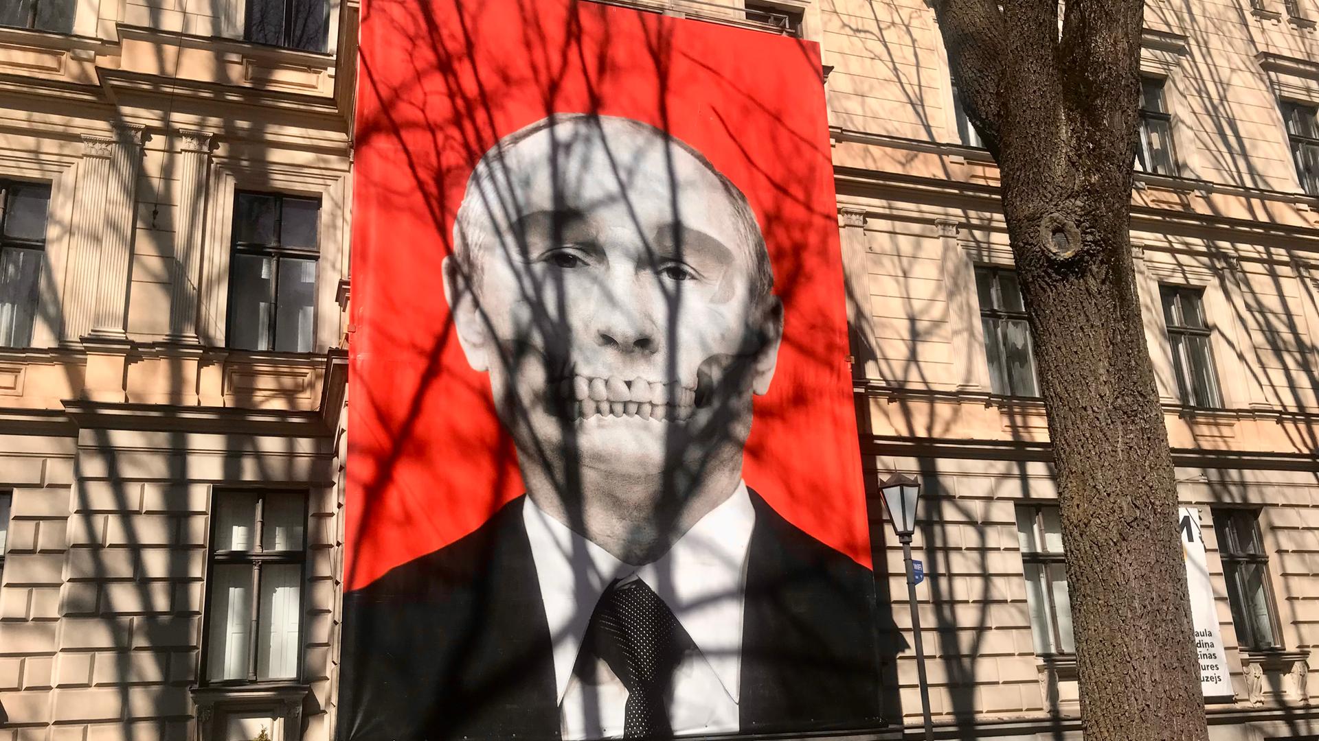 An der Fassade eines großen Gebäudes ist Putins Kopf auf rotem Hintergrund abgebildet, das Gebiß ähnelt einem Totenkopf.