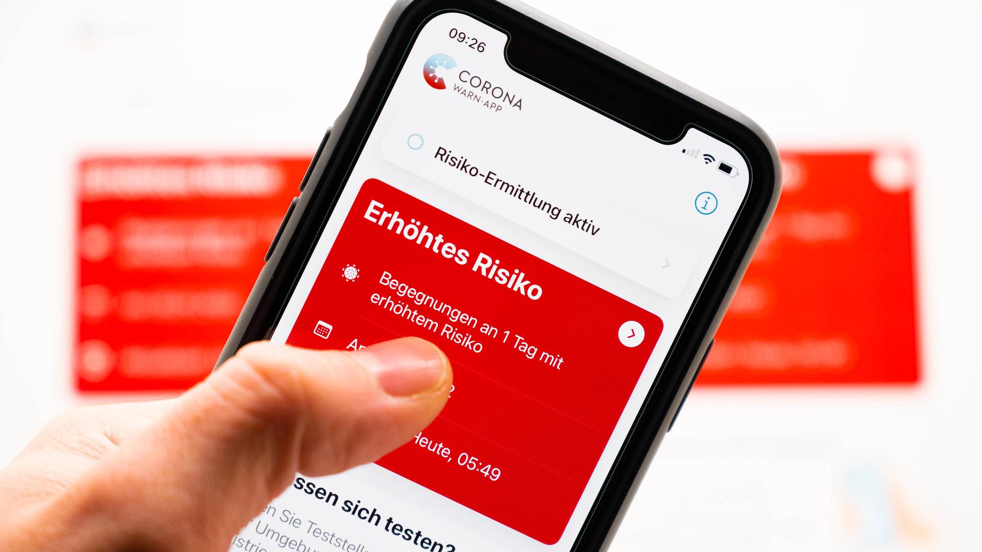 Eine Hand tippt auf ein Handydisplay. Dort ist das Symbol der Corona-Warn-App zu sehen-