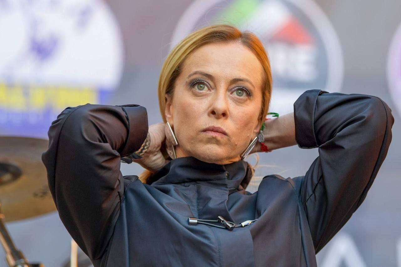 Eine blonde Frau in blauem Regencape und silbernen Ohrringen fasst sich mit beiden Händen in die Haare. Eine blonde Frau in blauem Regencape und silbernen Ohrringen fasst sich mit beiden Händen in die Haare.