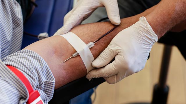 Ein Mitarbeiter befestigt eine Kanüle an dem Arm eines Mannes um eine Blutspende zu entnehmen