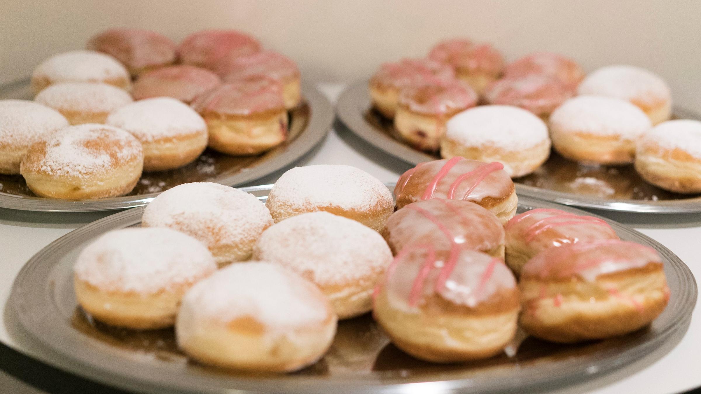 Auf drei silbernen Tabletts liegen jeweils acht runde gezuckerte Sufganyot (Krapfen) beim jüdischen Fest Chanukka. Auf drei silbernen Tabletts liegen jeweils acht runde gezuckerte Sufganyot (Krapfen) beim jüdischen Fest Chanukka.