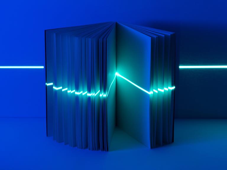 Ein geöffnetes Buch mit einem Lichtstrahl wie ein Laser, quer durch alle Seiten.