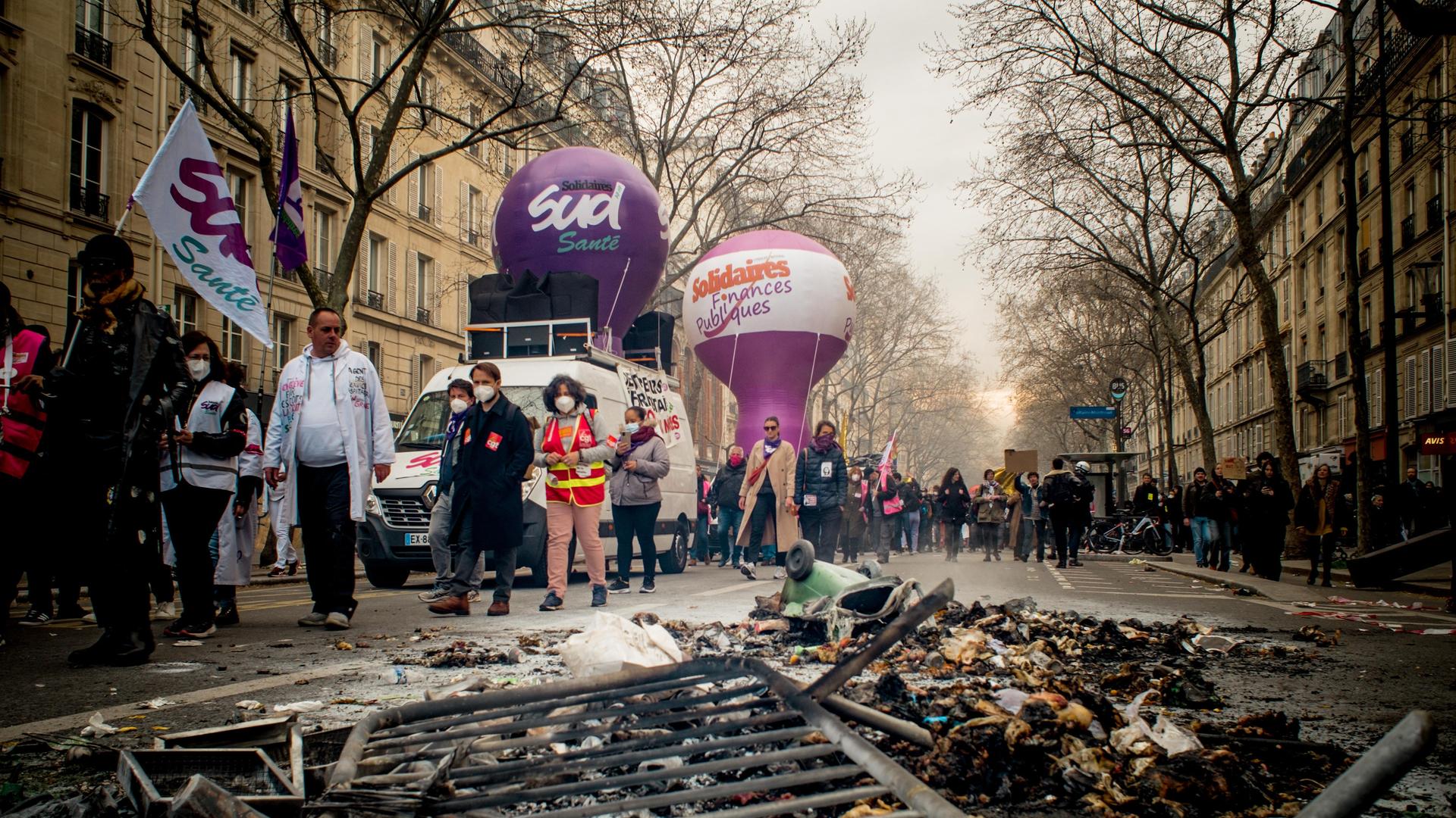 Ein Demonstrationszug in Paris, im Vordergrund des Bildes reste eines Brandes und ein liegendes Absperrgitter. Ein Demonstrationszug in Paris, im Vordergrund des Bildes reste eines Brandes und ein liegendes Absperrgitter.