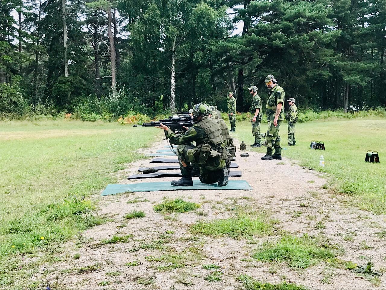 Frauen und Männer knien in militärischer Tarnkleidung auf Matten auf einer Wiese, die Gewehre im Anschlag. Ihre Trainer stehen hinter ihnen. Frauen und Männer knien in militärischer Tarnkleidung auf Matten auf einer Wiese, die Gewehre im Anschlag. Ihre Trainer stehen hinter ihnen.