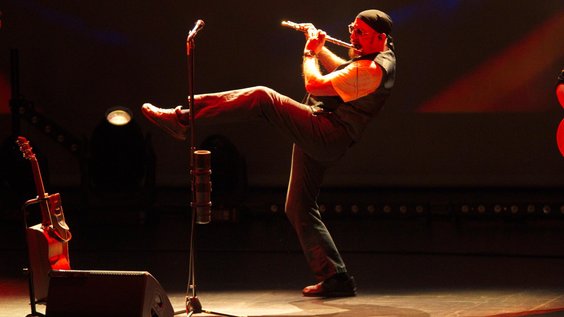 Ian Anderson steht auf einem Bein und spielt Querflöte auf der Bühne.