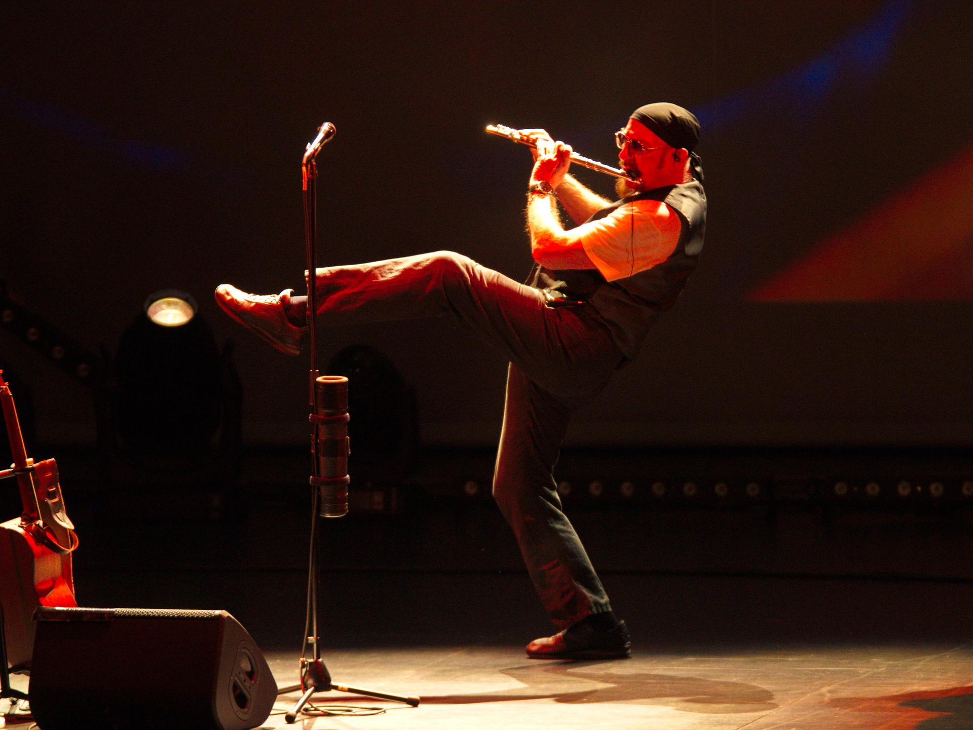 Ian Anderson steht auf einem Bein und spielt Querflöte auf der Bühne.