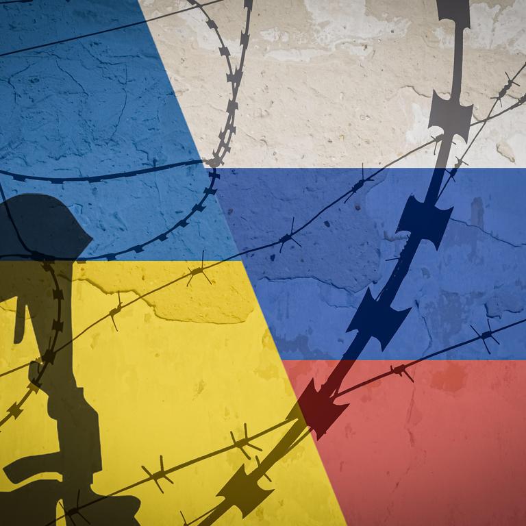 Schatten von Militärhelm, Maschinengewehr und Stacheldraht vor einer in den Farben der Ukraine und Russlands bemalten Wand
