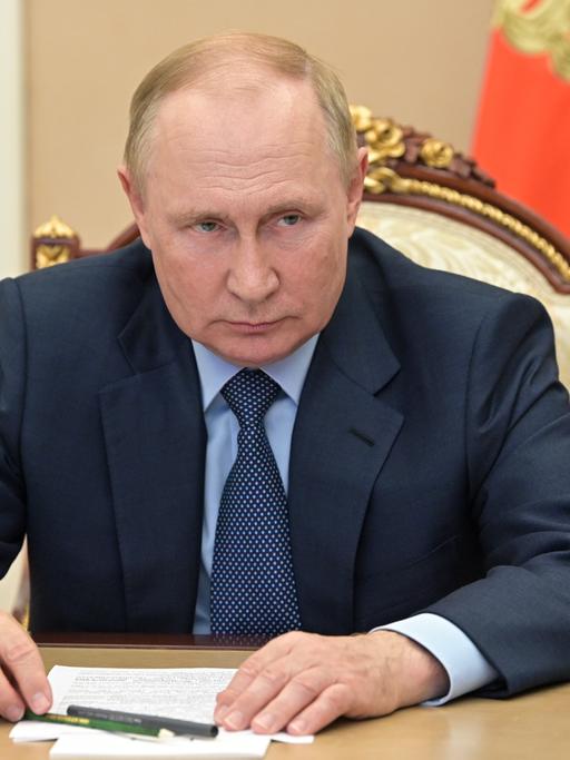 Wladimir Putin sitzt vor zwei Flaggen an einem Tisch.