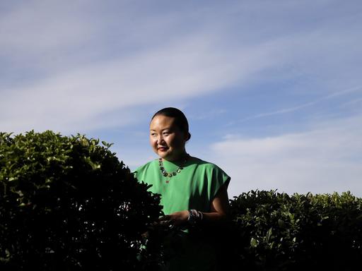 Hanya Yanagihara steht in grüner Bekleidung vor dem blauen Himmel hinter einer Hecke.