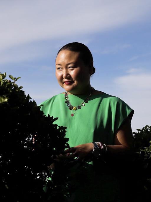 Hanya Yanagihara steht in grüner Bekleidung vor dem blauen Himmel hinter einer Hecke.