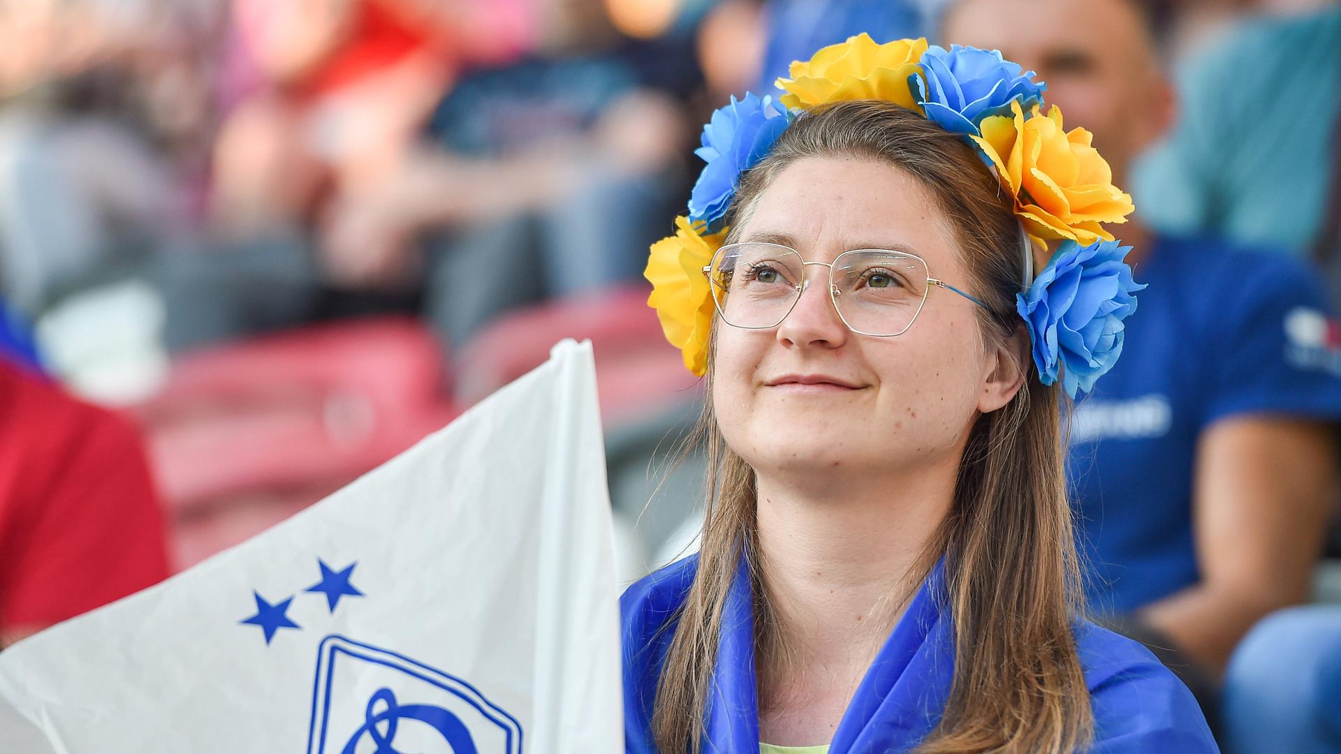 Eine Frau mit gelb-blauem Haarkranz, Flagge um die Schulter und Dynamo-Kiew-Wimpel-Fähnchen.