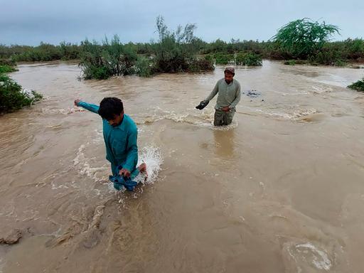 Dorfbewohner gehen durch die Fluten, die nach dem Monsunregen in Pakistan entstanden sind. 
