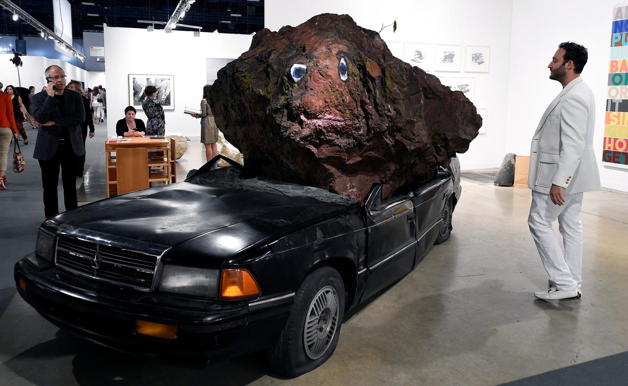Ein großer brauner Steinbrocken liegt auf dem eingedrückten Dach einer schwarzen Limousine. Ein großer brauner Steinbrocken liegt auf dem eingedrückten Dach einer schwarzen Limousine.