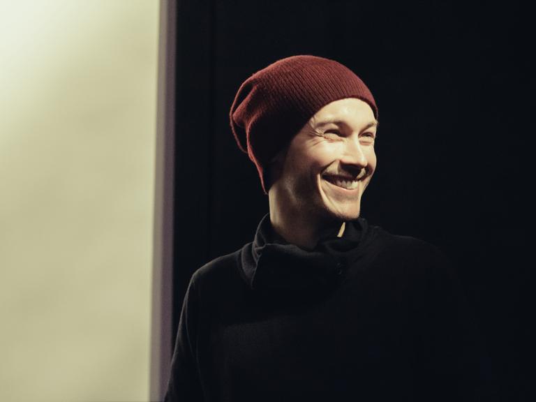 Der Drehbuchautor und Regisseur Benjamin Gutsche im Porträt. Er trägt eine Wollmütze und einen schwarzen Rollkragenpulli und lacht.