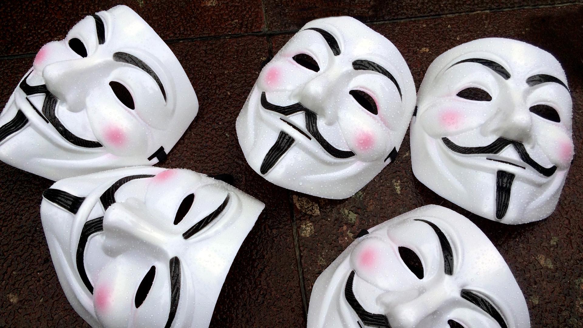 Fünf Guy Fawkes-Masken - weißes Gesicht mit schwarzem Schnurrbart - liegen auf dem Boden. Die Masken sind das Markenzeichen des Hackerkollektivs Anonymous.