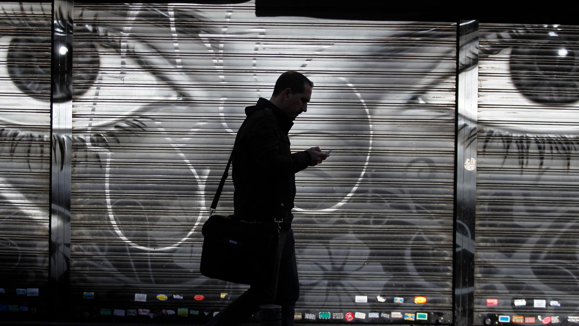 Ein Mann läuft mit seinem Handy auf einer Straße in Madrid. Im Hintergrund an der Wand sind große Augen gemalt. Ein Mann läuft mit seinem Handy auf einer Straße in Madrid. Im Hintergrund an der Wand sind große Augen gemalt.