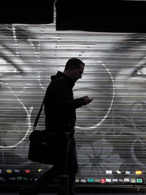 Ein Mann läuft mit seinem Handy auf einer Straße in Madrid. Im Hintergrund an der Wand sind große Augen gemalt.