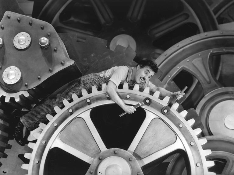 Charlie Chaplin liegt auf Zahnrädern im Stummfilm "Modern Times", 1936. 